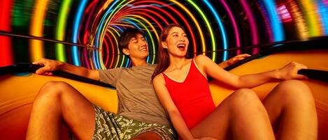 Duas pessoas sentadas numa superfície curva com uma instalação de luz circular e colorida ao fundo.