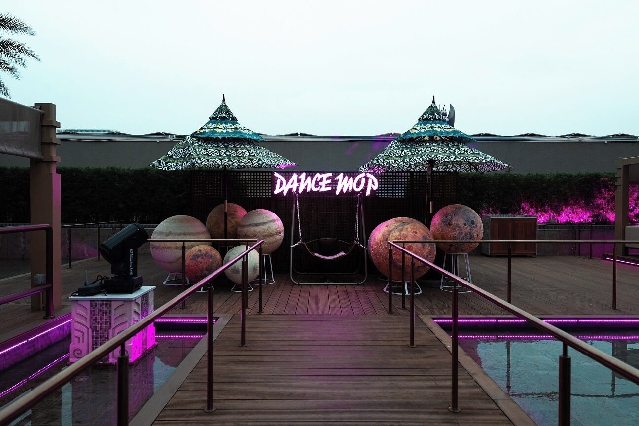 A poolside area with a neon sign reading "DANCE MOP," large decorative spheres, and a swing chair.