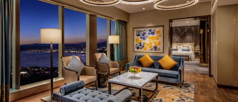 Una habitación de hotel moderna con vista a la ciudad, un conjunto de sofás, una mesa de comedor y una obra de arte grande en la pared.
