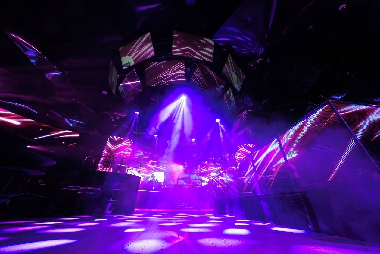A futuristic venue with a central stage, surrounded by geometric structures and purple lighting.
