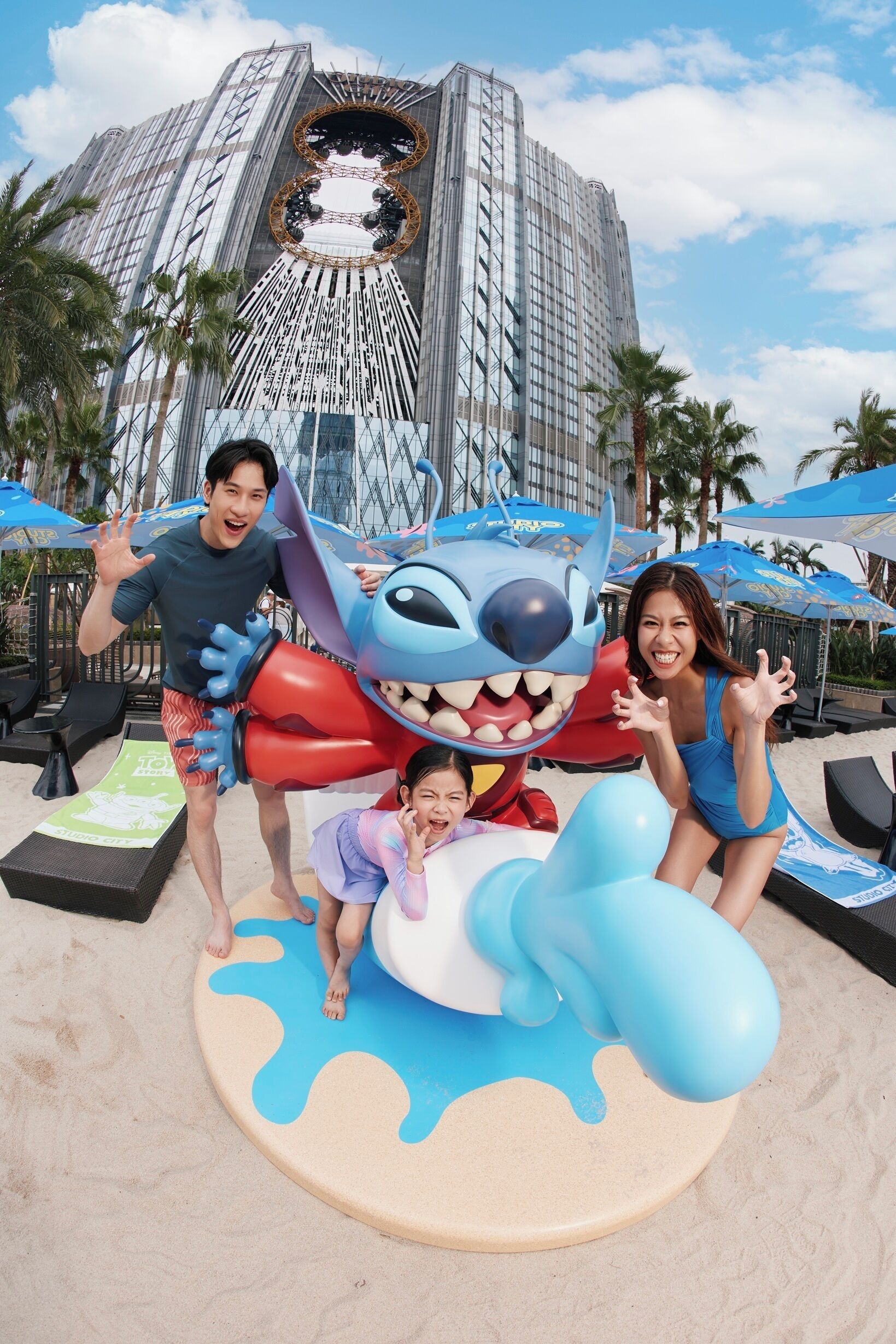 Una zona de playa con Stitch inflable y un edificio grande al fondo.