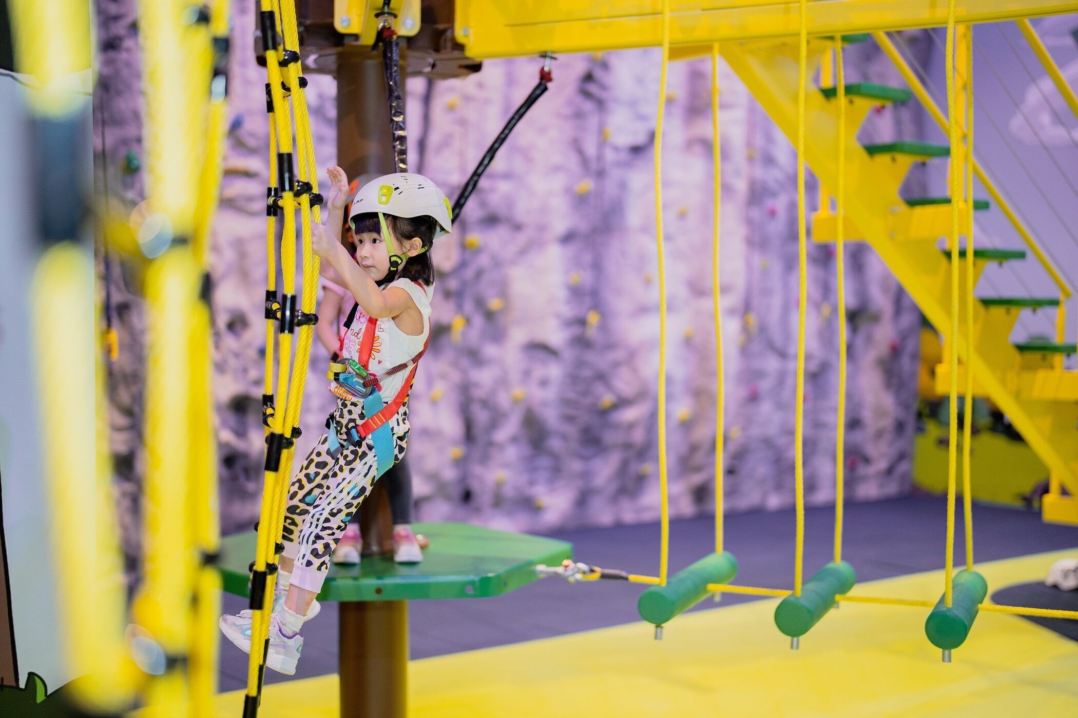 Un enfant escalade un parcours d’obstacles jaune sur fond violet.