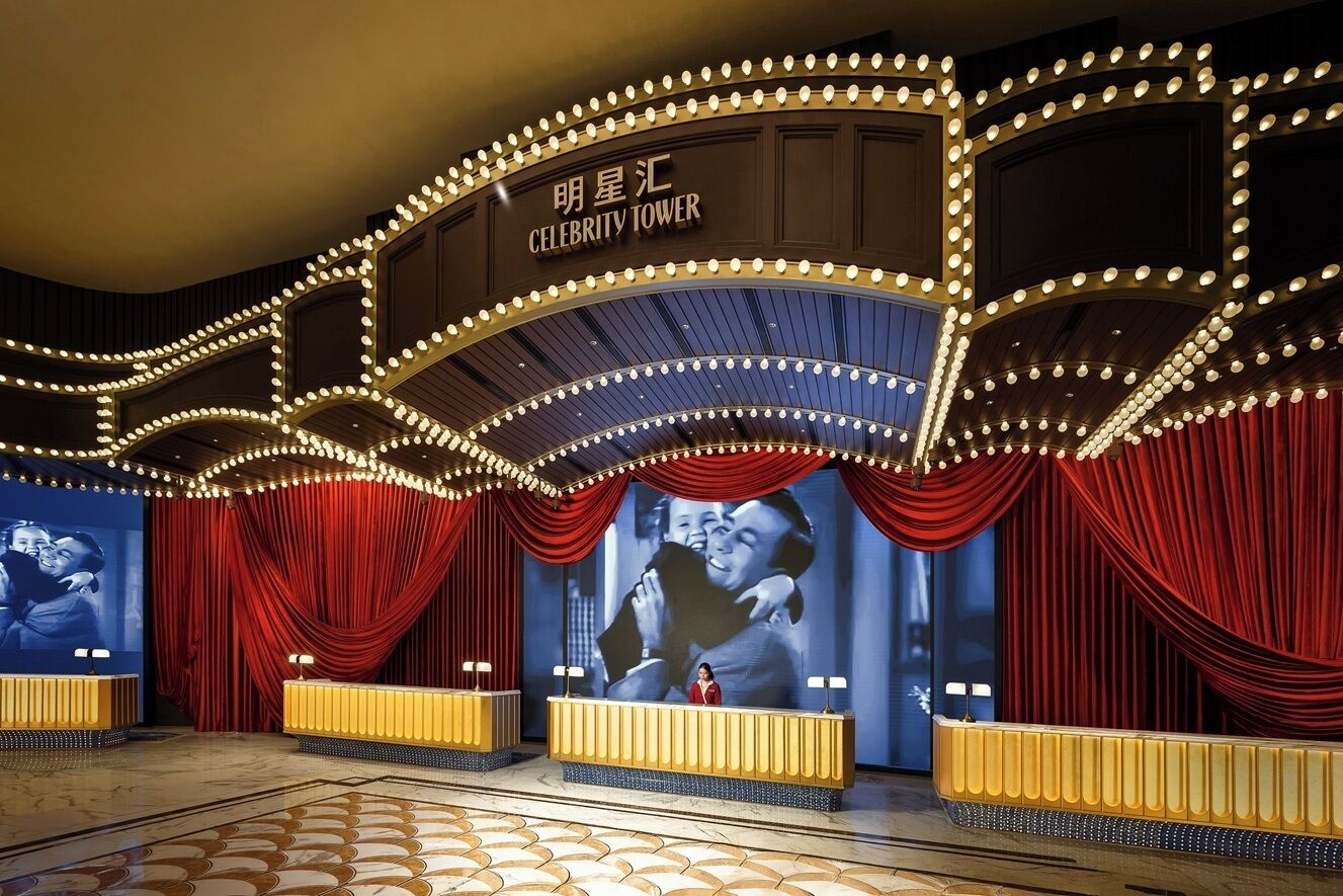 A theater with a red curtain backdrop, a stage with a single performer, and a sign reading "Celebrity Tower".