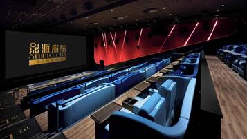 A cinema with rows of blue seats, a large screen, and a red wall with light fixtures.