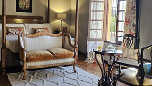Una habitación con cama con dosel, un sofá, suelo de madera y una ventana con cortinas.