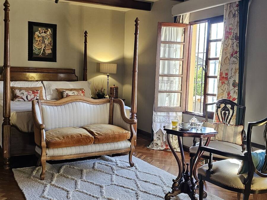 Una habitación con cama con dosel, un sofá, suelo de madera y una ventana con cortinas.