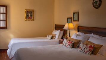 Habitación de hotel con dos camas, una mesita de noche con lámpara y cuadros en la pared.
