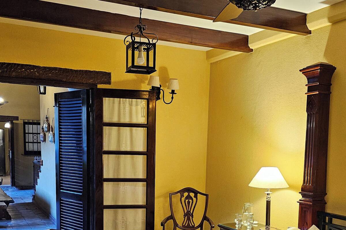 A bedroom with a wooden bed, a chair, a nightstand with a lamp, and a ceiling fan.