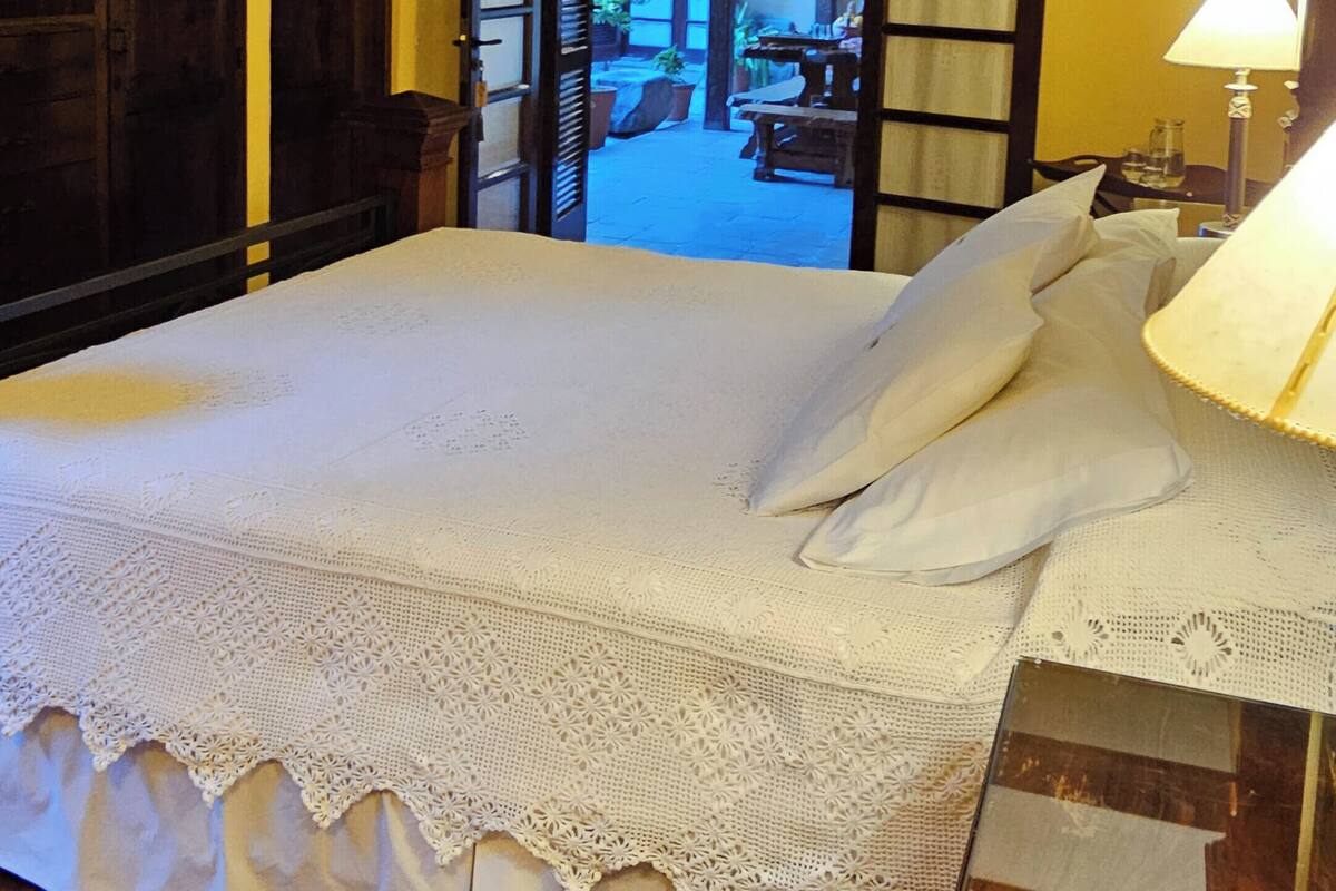 A bedroom with a large bed, wooden ceiling beams, and a view of an outdoor area through open doors.
