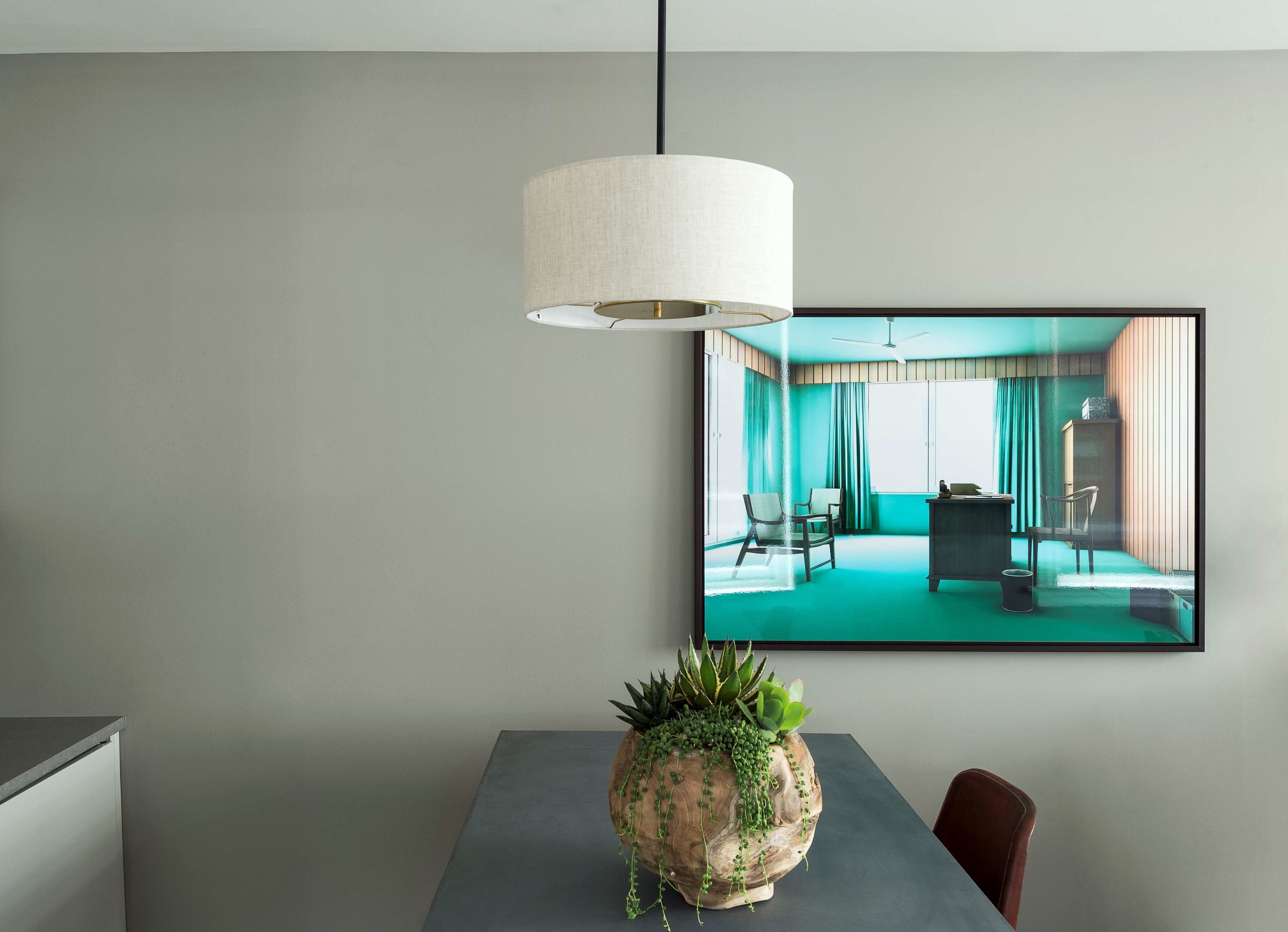 Een moderne kamer met een grijze muur, een groot raam met gordijnen, een plafondventilator en een tafel met een potplant.