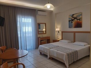 A hotel room with a bed, a desk, a chair, a lamp, and a painting on the wall. - Evagellina (Rethymno)