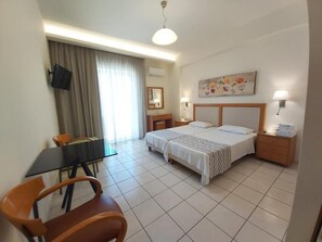 A hotel room with a bed, bedside tables, a desk with a chair, a television, and a painting on the wall. - Evagellina (Rethymno)