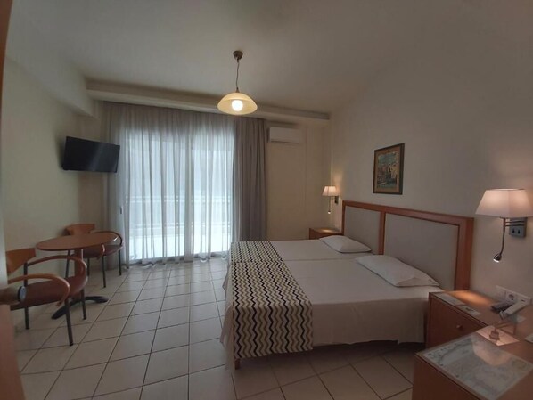 A hotel room with a bed, a desk, a chair, a television, and a window with curtains. - Evagellina (Rethymno)