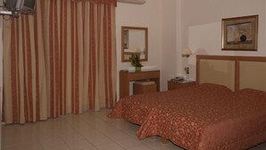 A hotel room with a bed, a bedside table, a mirror, a lamp, and curtains. - Evagellina (Rethymno)