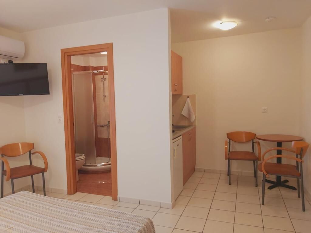 Een hotelkamer met een bed, een televisie, een douche, een kleine keuken en een eettafel met stoelen.