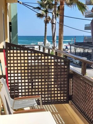 A balcony with a view of the beach, palm trees, and a fence. - Evagellina (Rethymno)