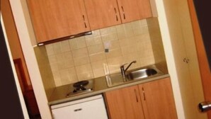 A compact kitchen with wooden cabinets, a tiled backsplash, and a built-in sink. - Evagellina (Rethymno)