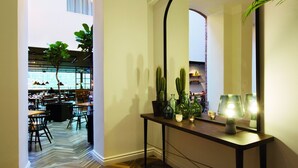 A modern interior with a herringbone wood floor, a console table with green plants and a lamp, and a large mirror reflecting the room. - Elite Hotel Mimer (Umea)