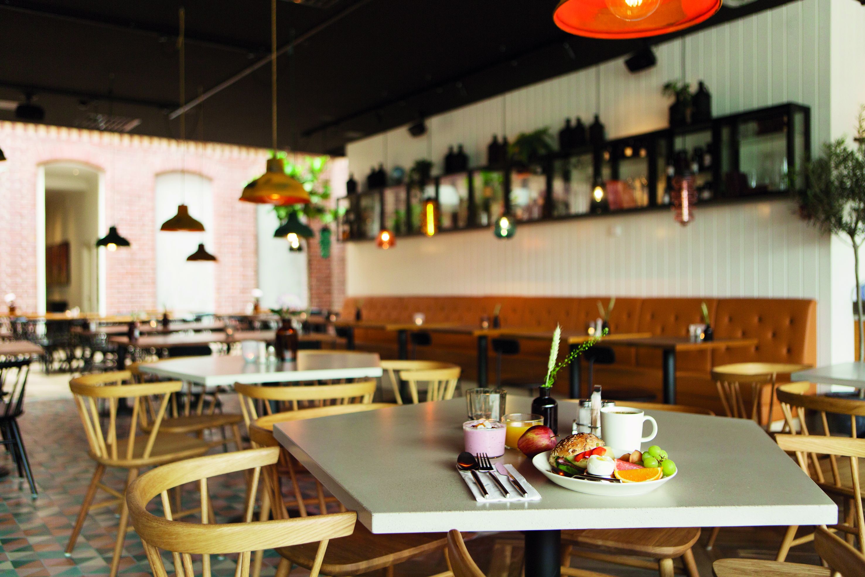 Interior de un restaurante con sillas y mesas de madera, y lámparas colgantes.