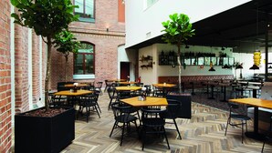 An indoor dining area with brick walls, wooden tables, and black chairs. There are potted plants and hanging lights. - Elite Hotel Mimer (Umea)