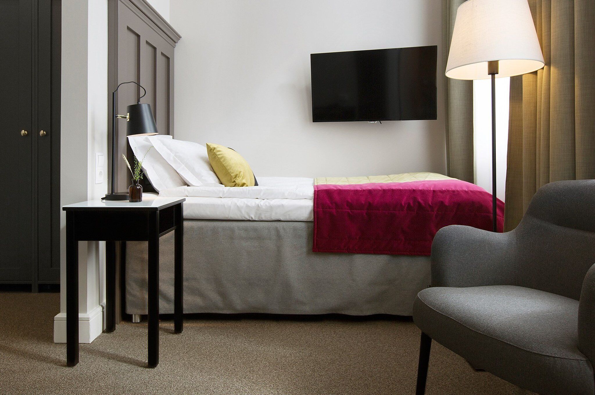 A hotel room with a bed, a desk, a chair, a TV, and a lamp.