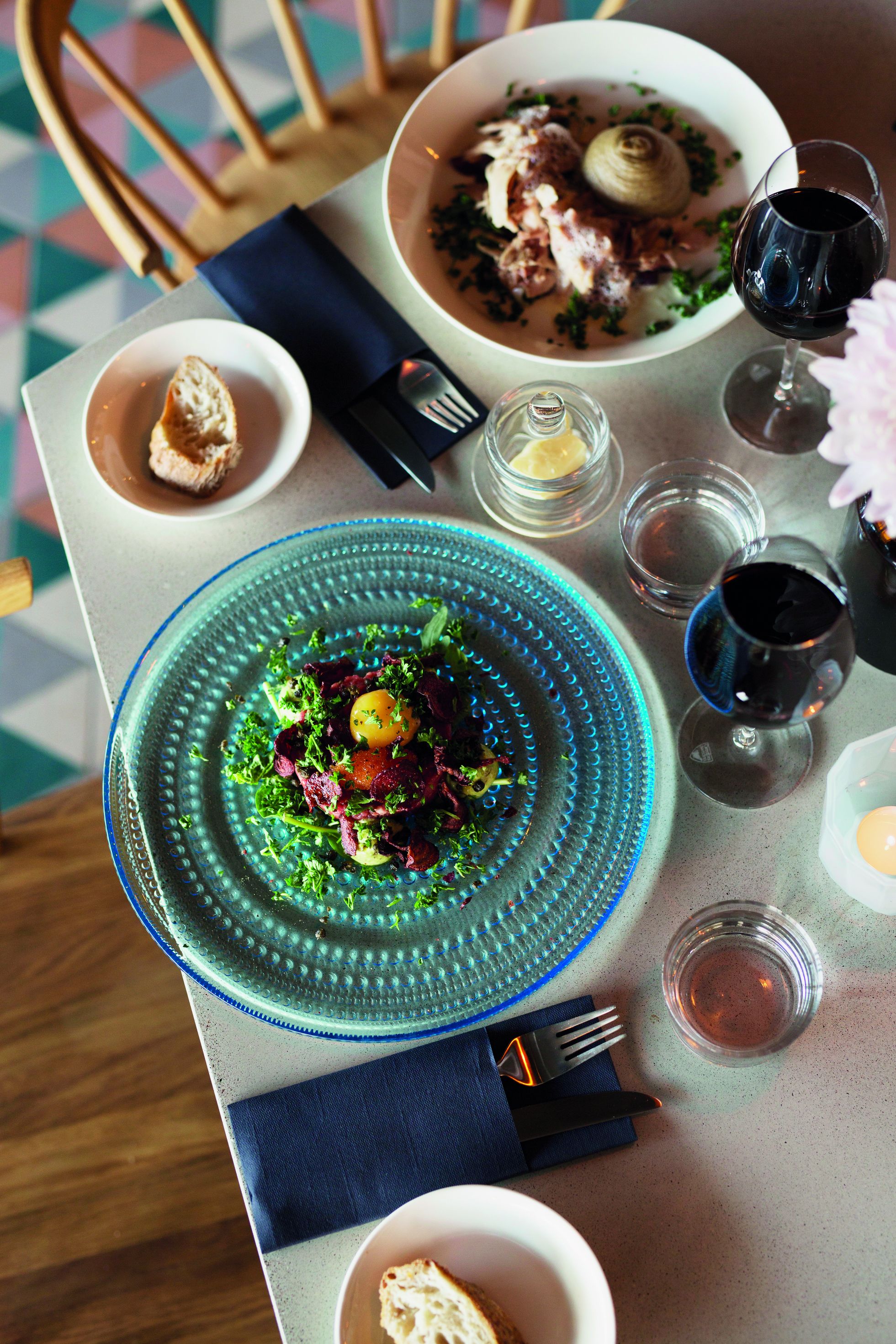 A dining table with a blue glass plate, a bowl of salad, and a glass of red wine.