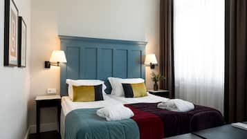 Habitación de hotel con dos camas, cabecero azul, lámparas de noche, una mesita y una ventana con cortinas.