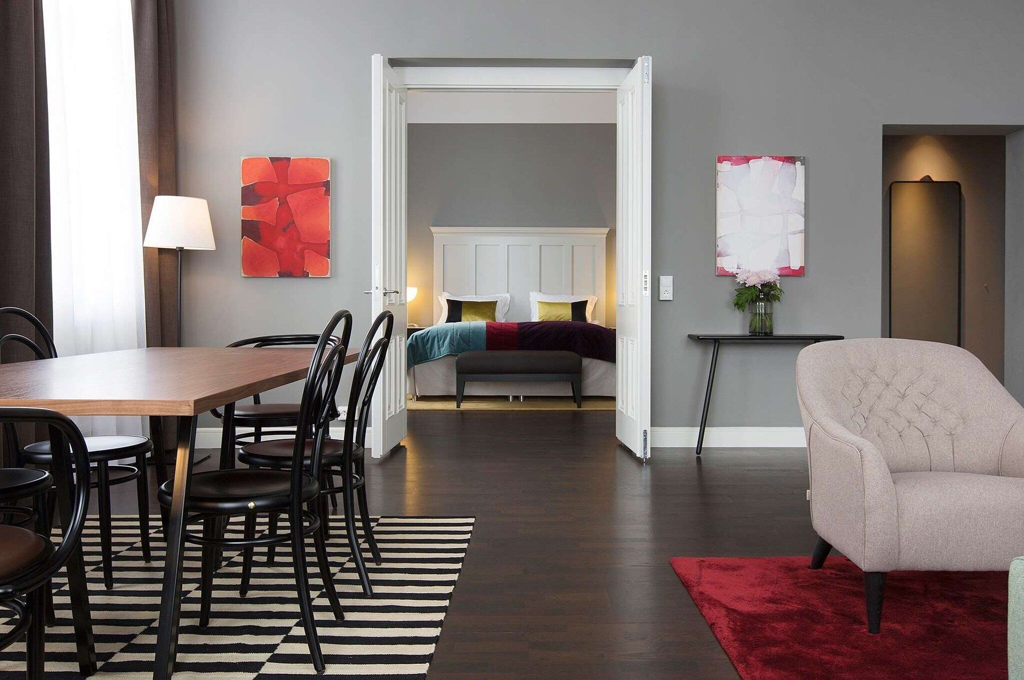 Una habitación de hotel moderna con zona de comedor, una cama con cabecera y una sala de estar con una silla y una mesa.