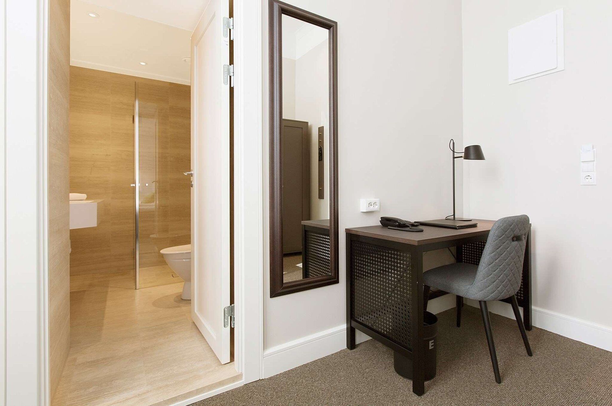 Un baño moderno con mampara de vidrio, inodoro y un espejo grande.