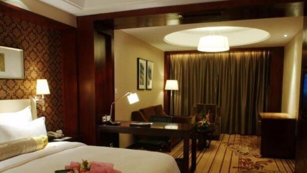 Une chambre d’hôtel avec un grand lit, un bureau avec une lampe, une chaise et un sol recouvert de moquette.