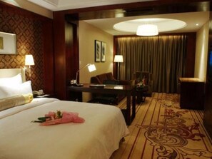Une chambre d’hôtel avec un grand lit, un bureau avec une lampe, une chaise et un sol recouvert de moquette.