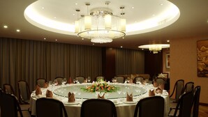 Une salle à manger élégante, avec une table ronde dressée pour un repas, entourée de chaises, et un grand lustre au-dessus.