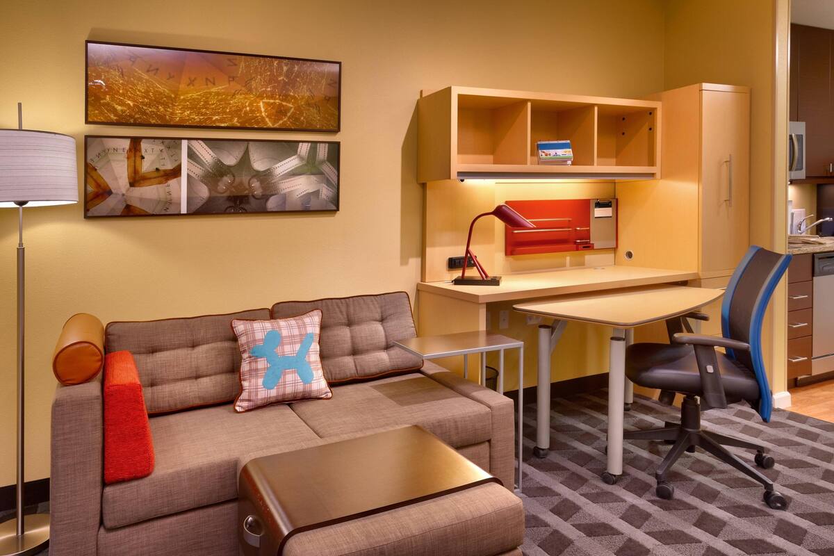 Une chambre d’hôtel moderne équipée d’un canapé, d’un bureau, d’une chaise, d’une lampe et d’un meuble de rangement.