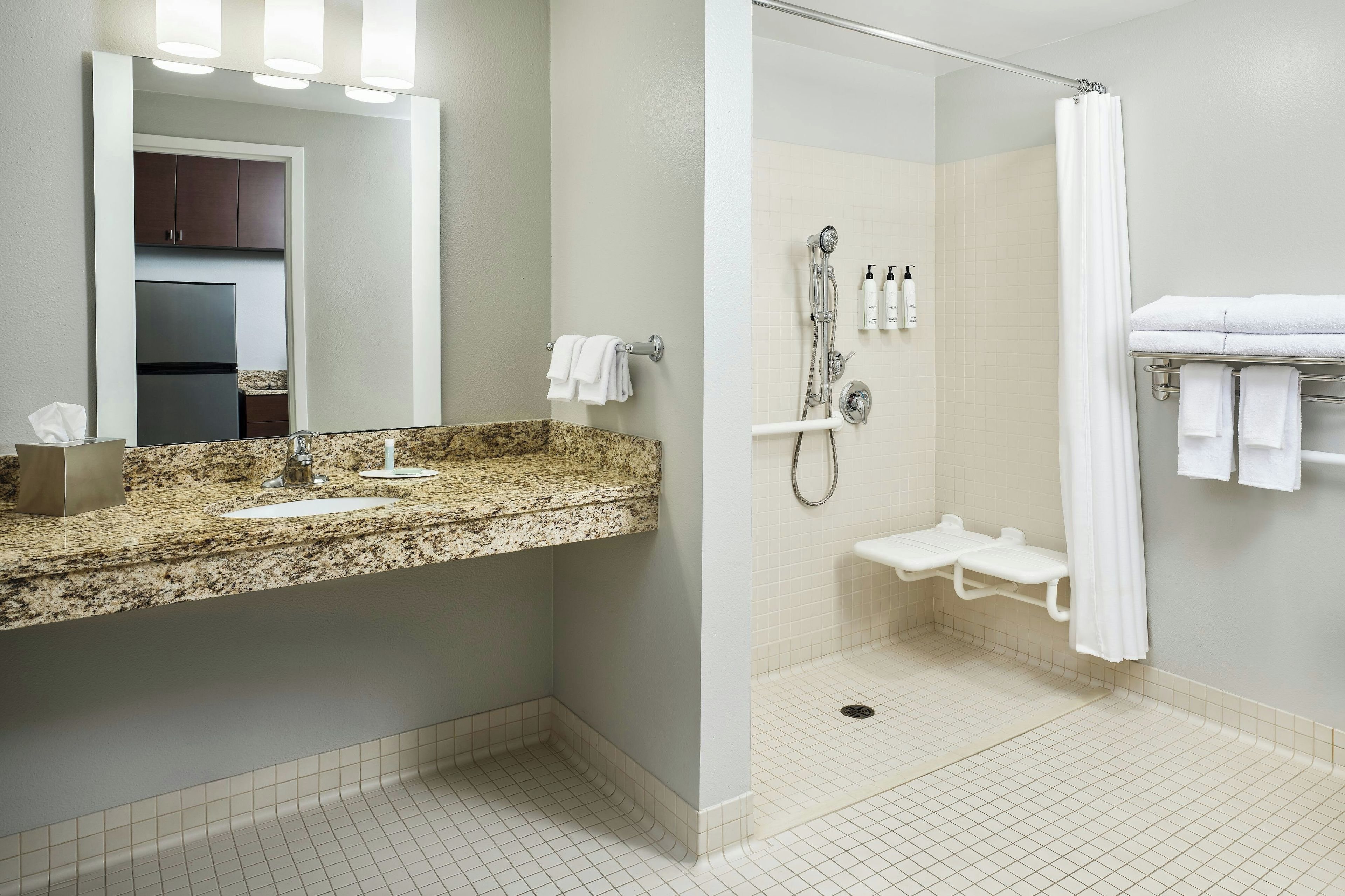 A bathroom with a granite countertop sink, a mirror, a shower with a handheld showerhead, and a towel rack.