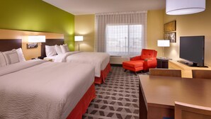 Quarto de hotel com duas camas, uma cadeira vermelha, uma televisão e uma janela com cortinas.