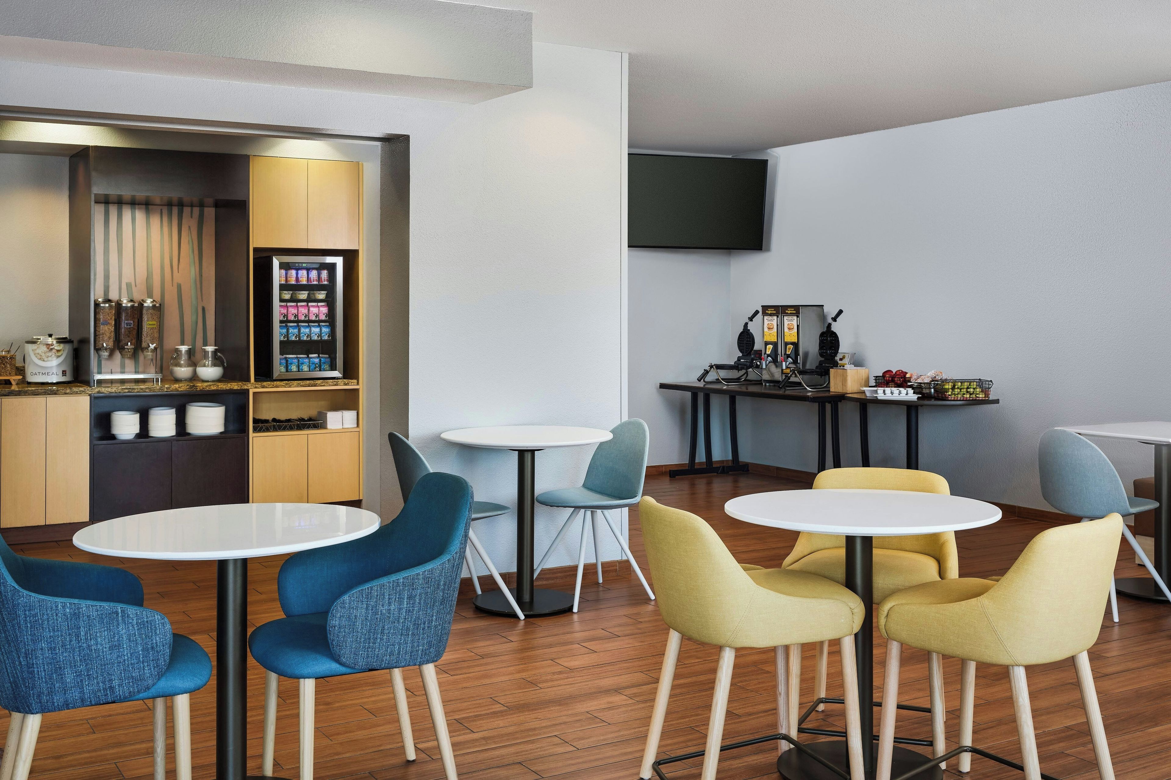 A modern lounge area with round tables and chairs, a coffee machine, and a snack vending machine.