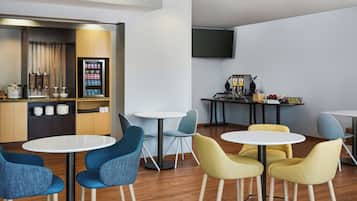 A modern lounge area with round tables and chairs, a coffee machine, and a snack vending machine.
