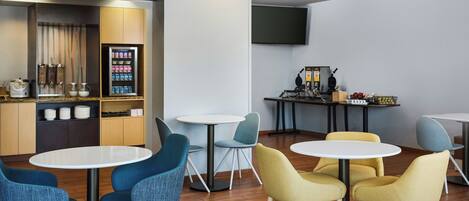 A modern lounge area with round tables and chairs, a coffee machine, and a snack vending machine.