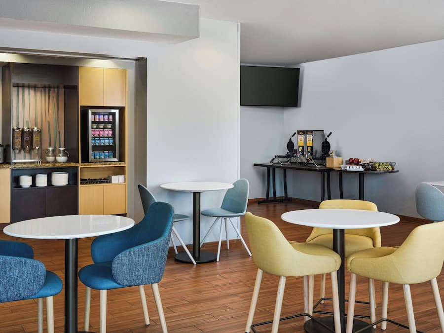 A modern lounge area with round tables and chairs, a coffee machine, and a snack vending machine.