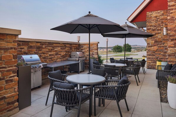 An outdoor patio with a grill, seating, and a view of the landscape.