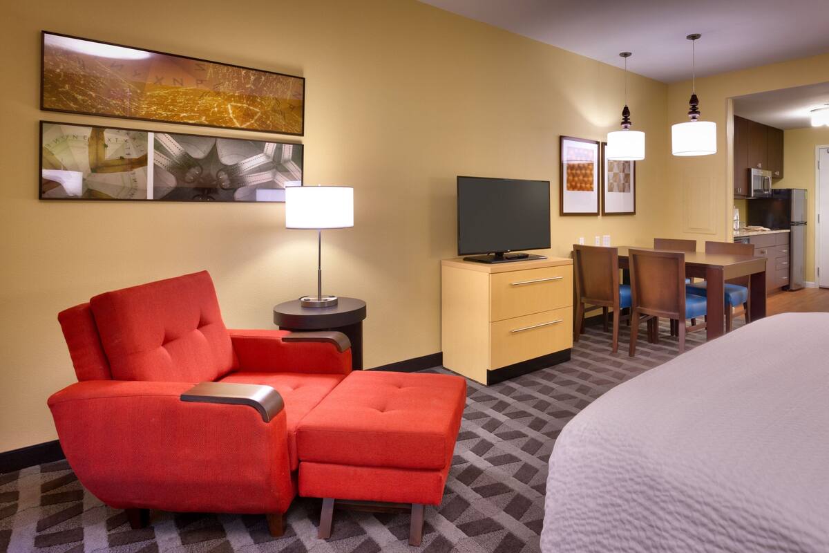 Une chambre d’hôtel avec un fauteuil rouge, une télévision, un bureau avec une chaise et un lit.