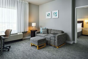 Et hotelværelse med sofa, skærmer, et lille bord, en stol, en lampe og et natbord.