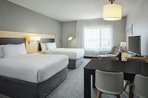 Een hotelkamer met twee bedden, een bureau met een stoel, een lamp en een groot raam met dunne gordijnen.