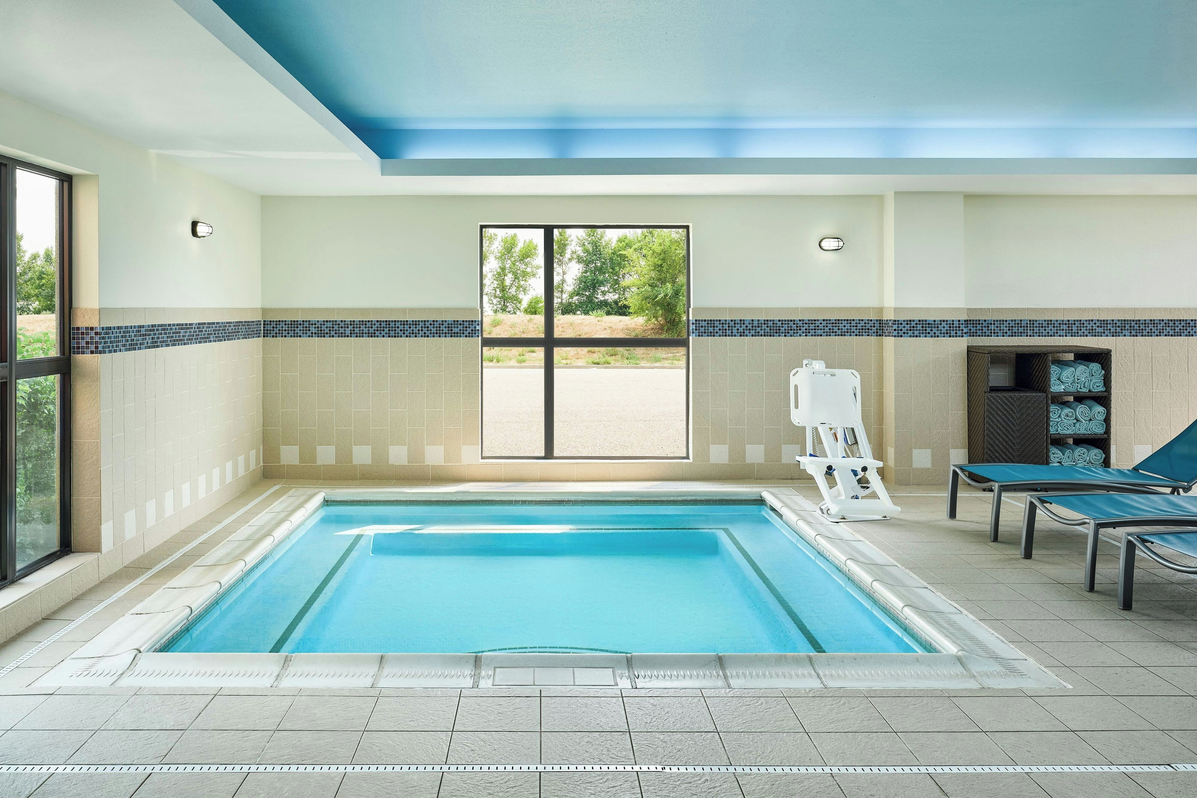 An indoor swimming pool with a view of the outdoors through a large window.