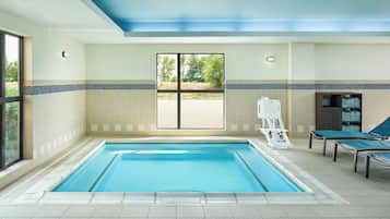 An indoor swimming pool with a view of the outdoors through a large window.