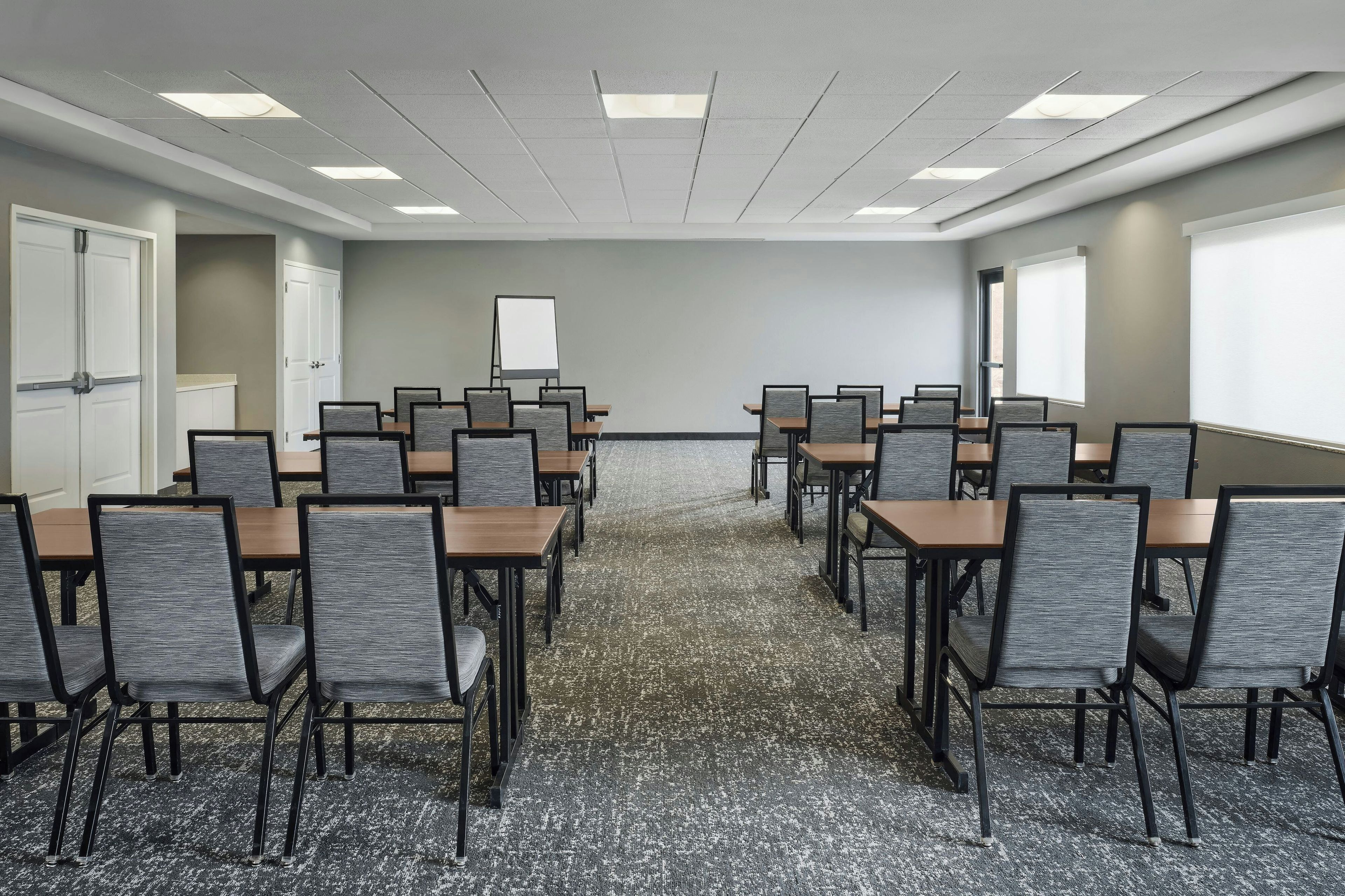 A conference room with multiple tables and chairs, a whiteboard, and a carpeted floor.