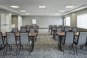 Un salón de conferencias con varias mesas y sillas, una pizarra y piso alfombrado.