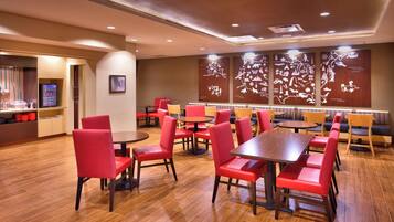 A restaurant with red chairs and tables, wooden flooring, and wall art depicting various scenes.