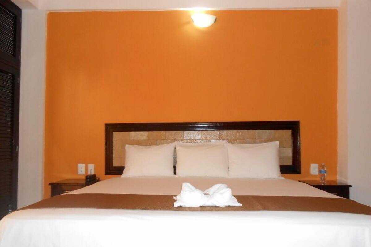 A hotel room with a large bed, a headboard with a stone-like texture, and a bright orange wall.