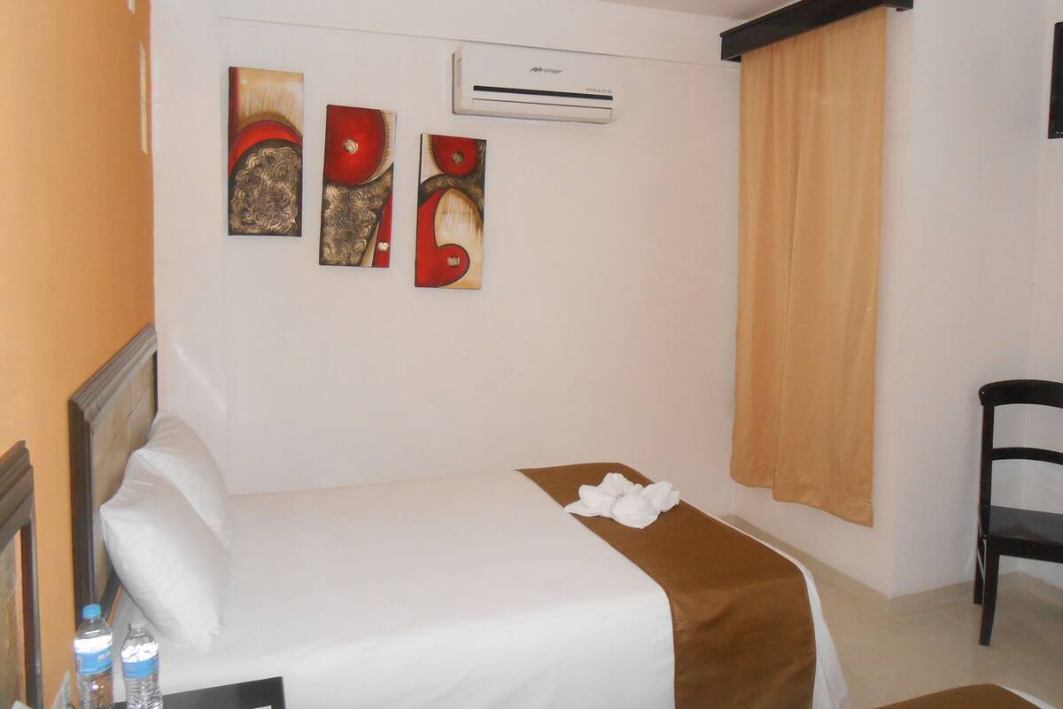 A hotel room with a bed, a chair, and three wall-mounted artworks.